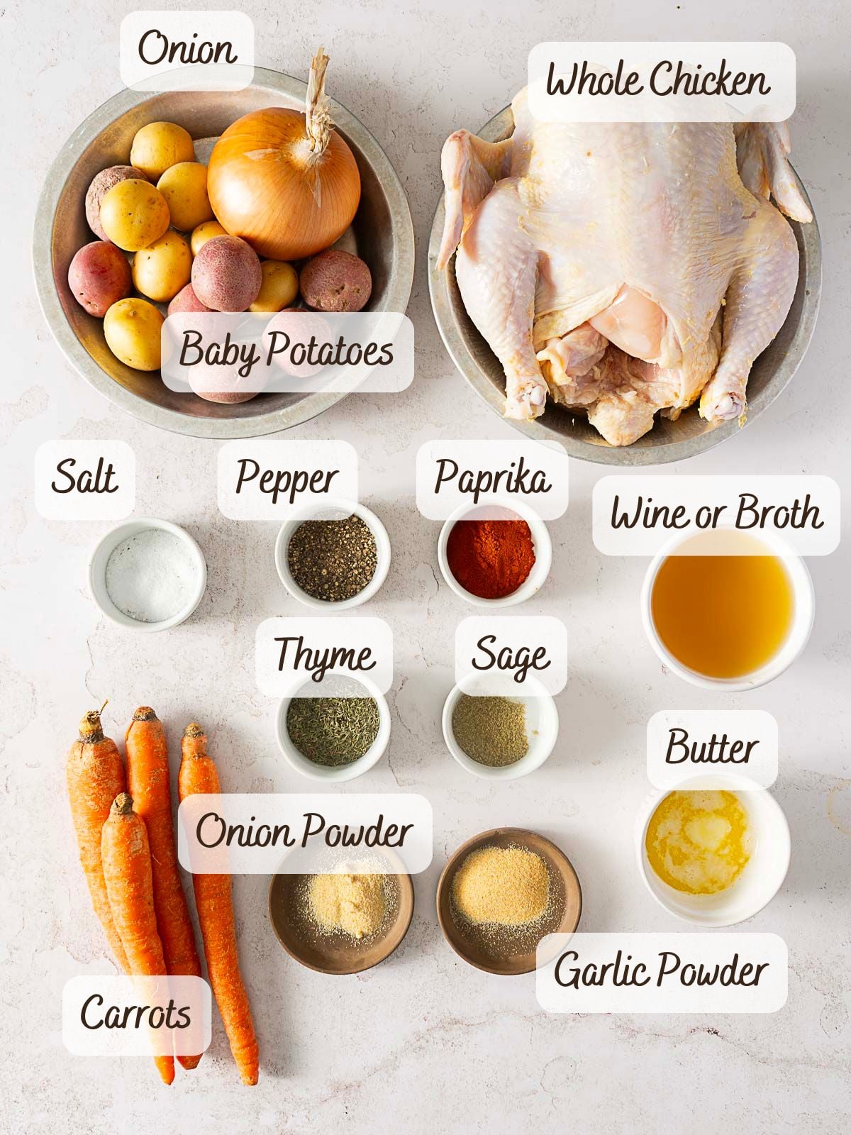A whole chicken, potatoes, carrots, onion, seasonings, butter, and broth or wine are arranged in separate bowls on a white surface-ingredients labeled for an easy bundt pan chicken recipe.