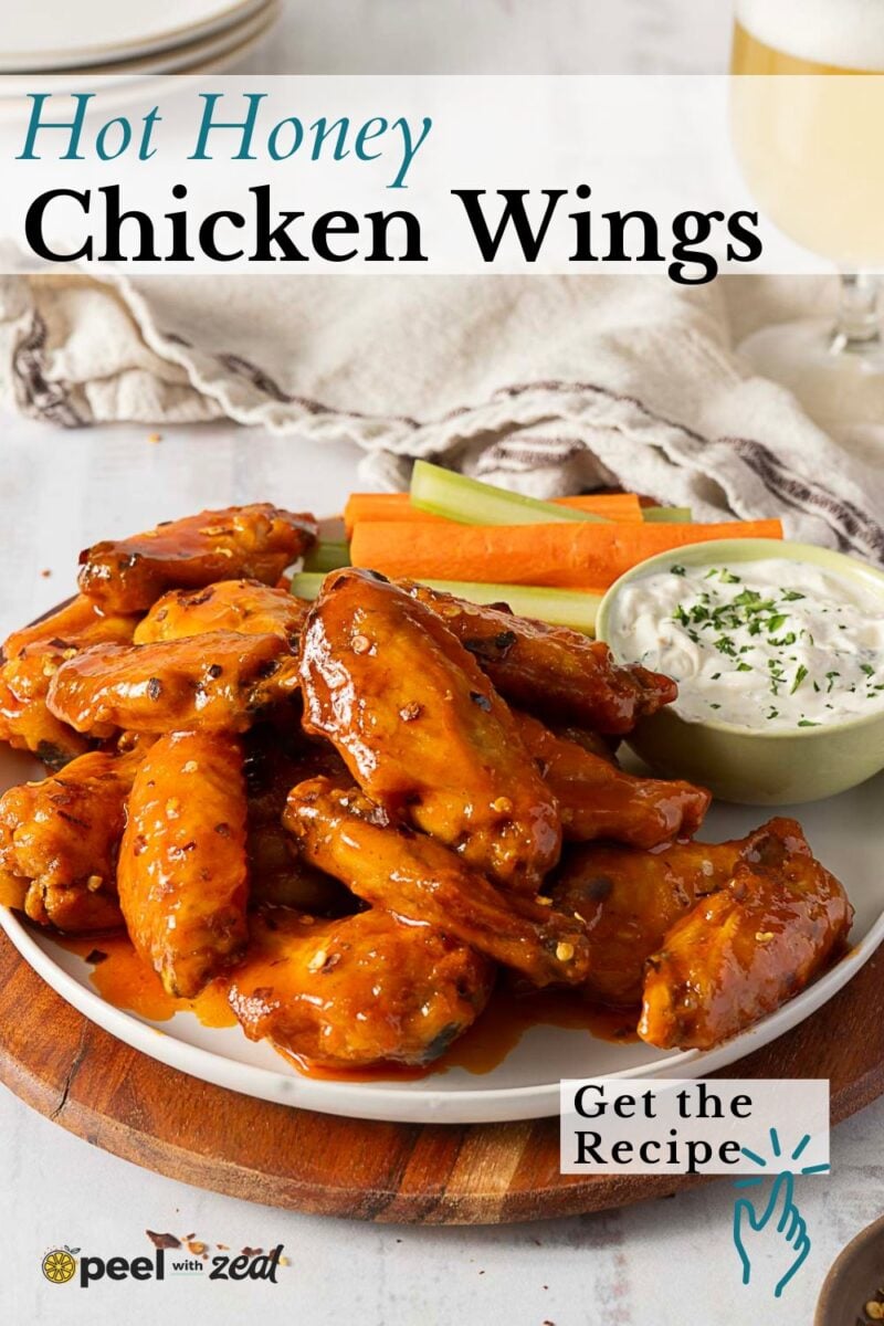 A plate of Hot Honey Buffalo Wings is served with celery and carrot sticks, alongside a bowl of ranch dip. A drink is partially visible in the background. Text on the image reads "Hot Honey Chicken Wings.