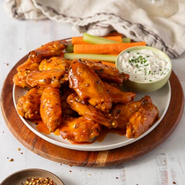 A plate of Hot Honey Buffalo Wings glazed to perfection, served with celery and carrot sticks, accompanied by a small bowl of ranch dipping sauce, on a wooden board.