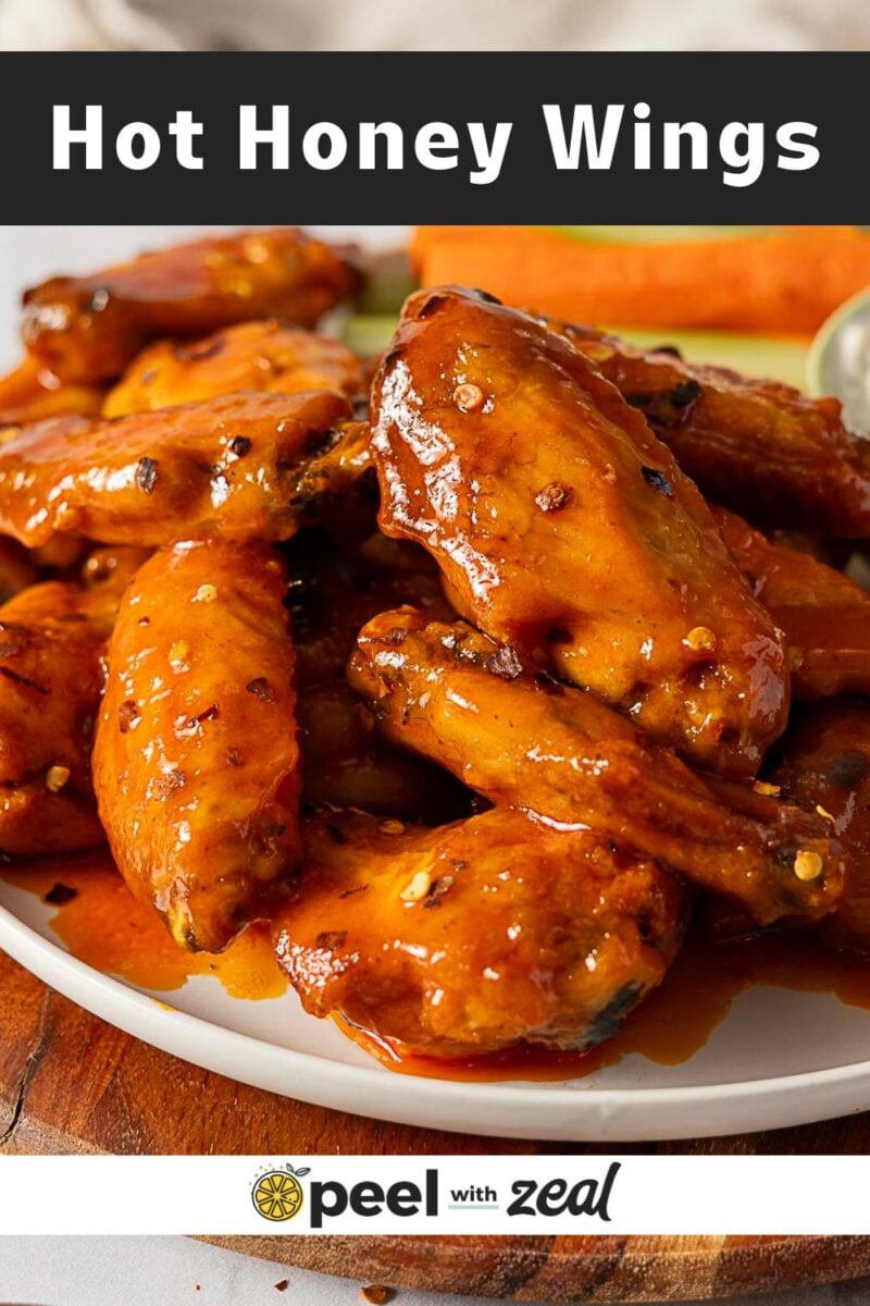 A plate of Hot Honey Buffalo Wings coated in a shiny, reddish-orange hot honey sauce, garnished with chili flakes. The text "Hot Honey Wings" appears at the top, with a "peel with zeal" logo at the bottom.