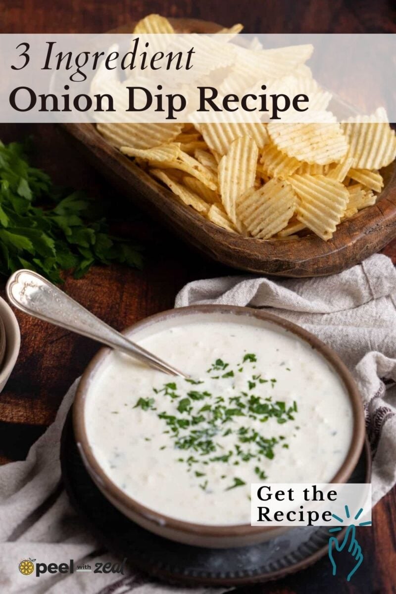 A bowl of onion dip garnished with chopped herbs sits next to a platter of ridged potato chips on a wooden table.
