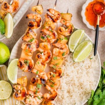 Shrimp Pineapple Skewers served with white rice, lime wedges, and a side of sweet chili sauce make a vibrant and flavorful meal.