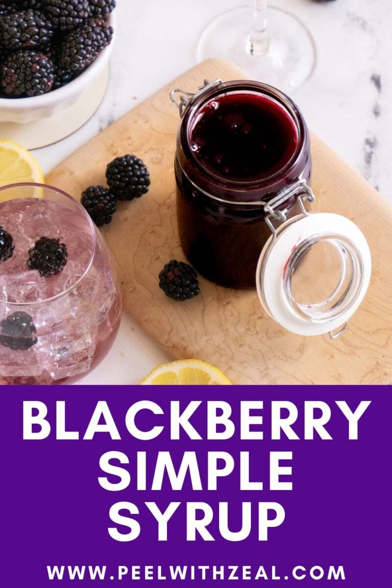 A jar of blackberry syrup sits on a wooden board next to a glass with ice and blackberries, lemon slices, and a bowl of blackberries. Text reads "Blackberry Simple Syrup.