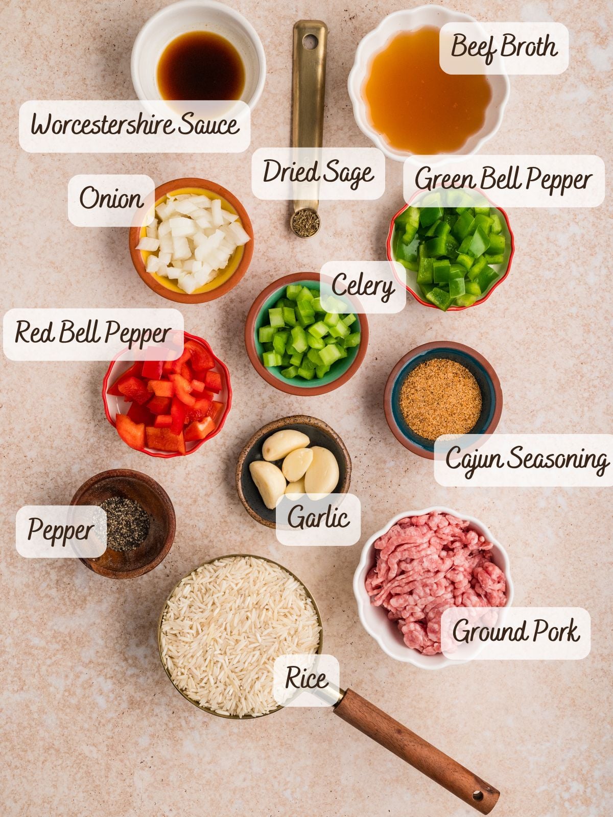 Top-down view of labeled dirty rice ingredients for a recipe, including ground pork, rice, vegetables, spices, garlic, beef broth, and Worcestershire sauce arranged on a light surface.
