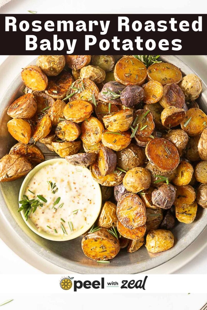 A bowl of roasted baby potatoes garnished with rosemary, served with a side of creamy dipping sauce. The text "Rosemary Roasted Baby Potatoes" appears at the top.