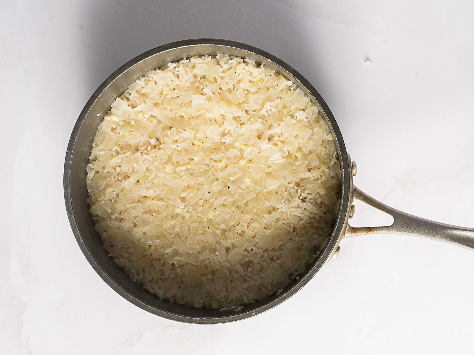 A saucepan filled with cooked, finely chopped onions on a white surface, perfect for starting a flavorful Greek Rice Pilaf.