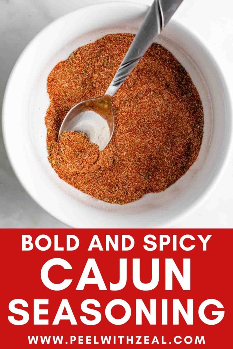 A bowl of Cajun seasoning mix with a spoon, placed above bold text that reads "Bold and Spicy Cajun Seasoning www.peelwithzeal.com".