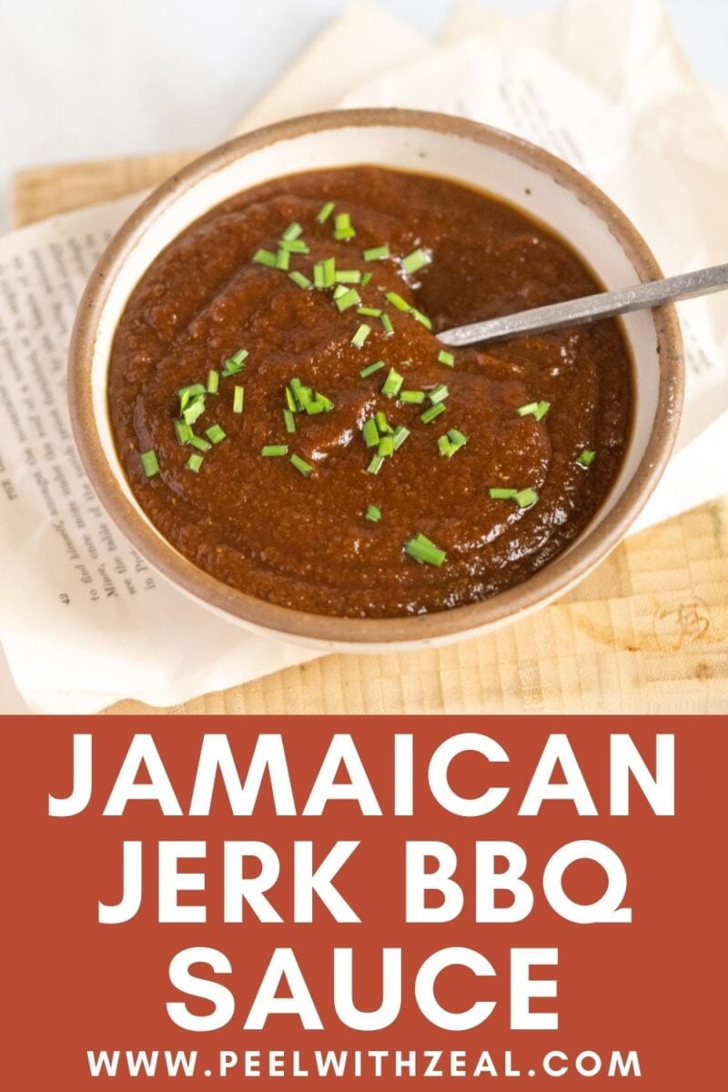 A bowl of Jamaican jerk BBQ sauce garnished with chopped chives, with a spoon in the bowl, set on a wooden surface.