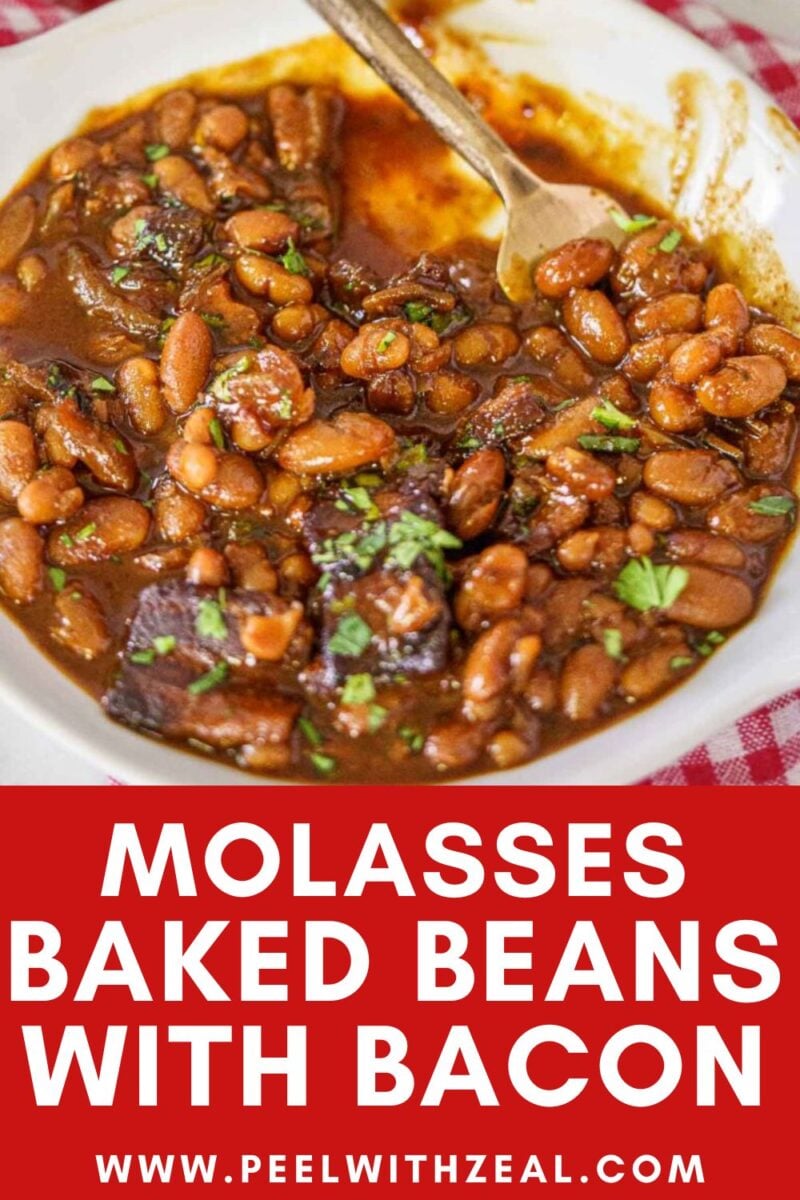 A bowl of molasses baked beans with pieces of bacon, garnished with chopped herbs, with a spoon in the dish.