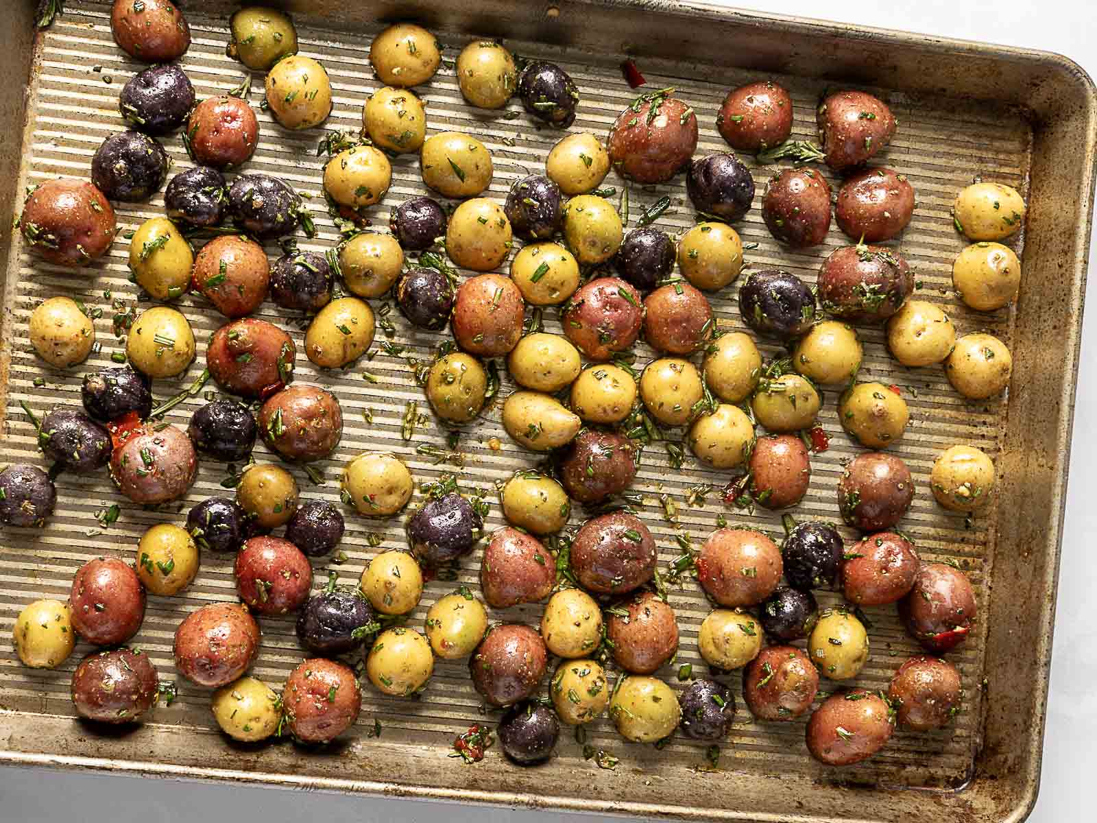 A baking sheet with crispy roasted baby potatoes, seasoned with fresh herbs and spices.