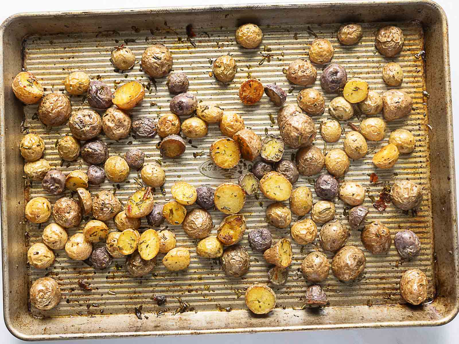 A baking sheet with crispy baby potatoes, some halved and some whole, perfectly seasoned and evenly spread out across the pan.