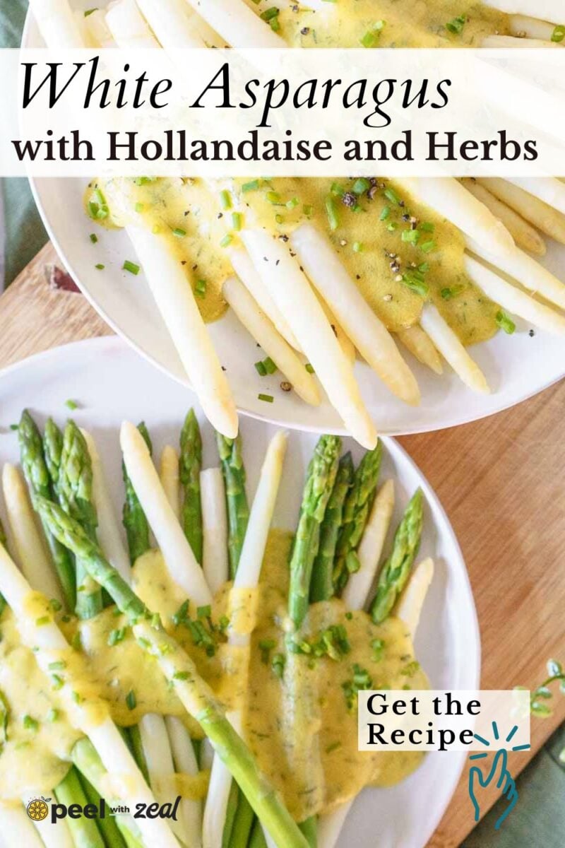Two plates of white and green asparagus topped with hollandaise sauce and chopped herbs, displayed on a wooden surface.