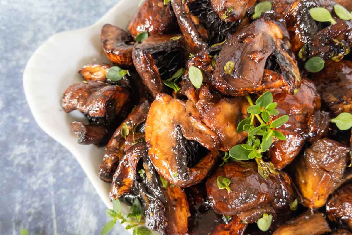 A close-up of roasted mushrooms garnished with fresh herbs, served in a white dish.