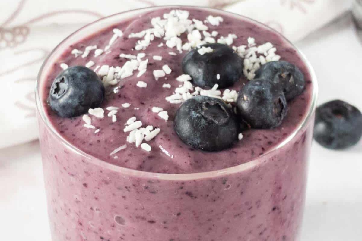 A glass filled with a thick blueberry smoothie, topped with fresh blueberries and shredded coconut.