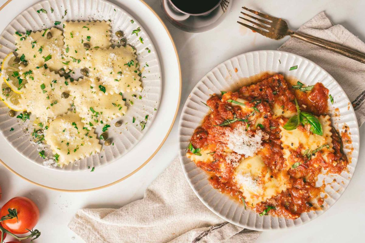 Two restaurant-worthy pasta dishes: ravioli with creamy white sauce and capers, and another with tomato sauce and basil, set on a table with a fork, napkin, and a glass of red wine.
