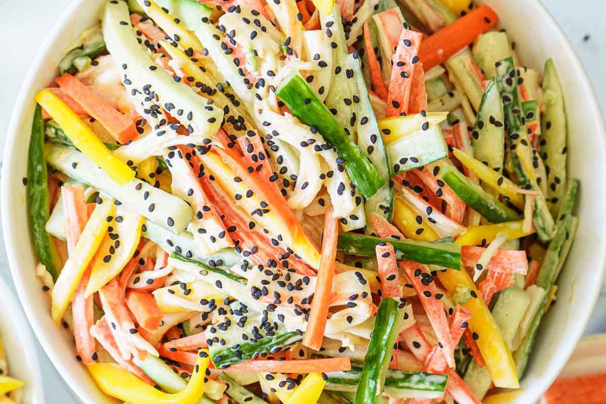 A bowl of julienned vegetables and imitation crab sticks mixed with creamy dressing, topped with black sesame seeds.
