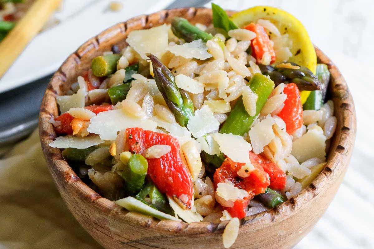 A wooden bowl filled with orzo pasta, asparagus, red peppers, and shaved parmesan cheese—perfect for holiday side dishes or as one of your favorite Easter sides.