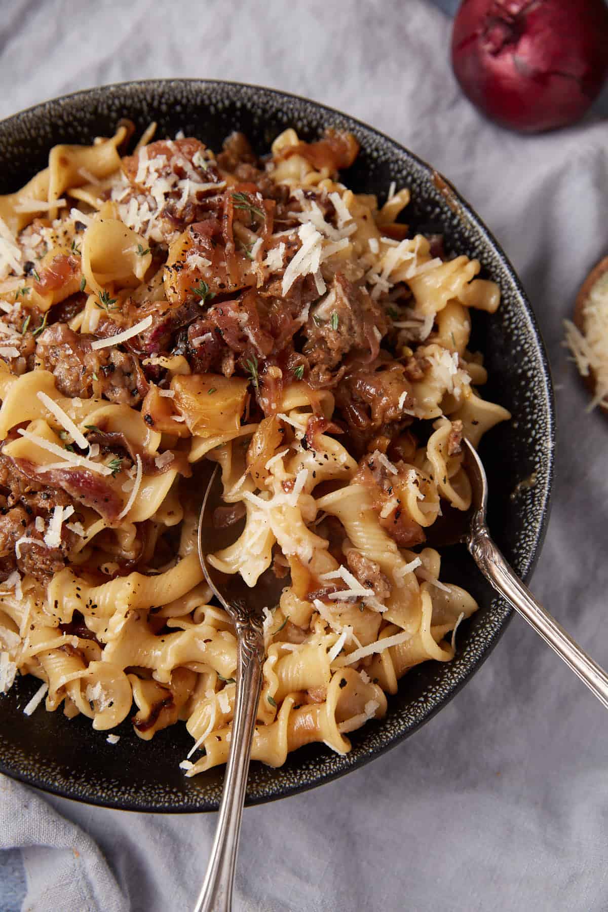 A black bowl filled with pasta topped with ground meat, sauce, and grated cheese, with two forks resting inside the bowl.