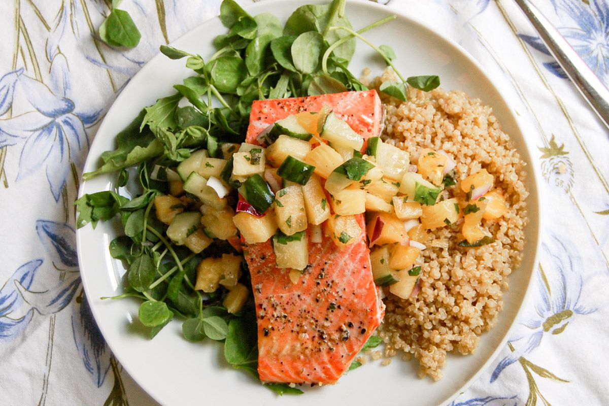 A plate with baked salmon topped with fruit salsa, served with quinoa and a side of leafy greens.