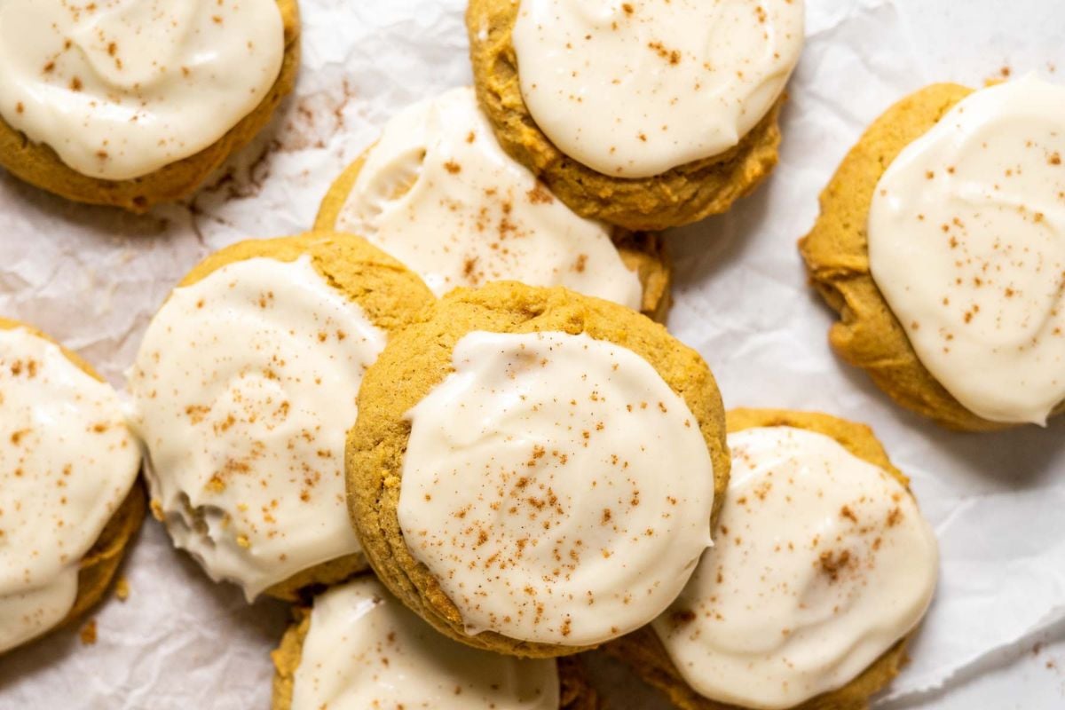 A group of frosted cookies topped with a sprinkle of spices, arranged on a piece of parchment paper.