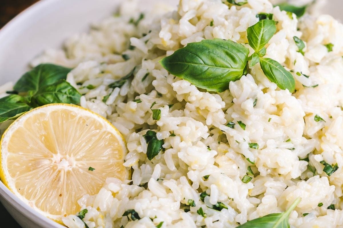 A bowl of cooked rice garnished with fresh basil leaves and a halved lemon.