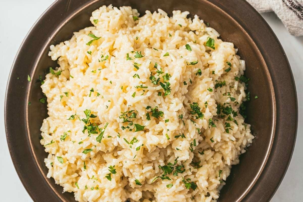 A brown bowl filled with creamy rice garnished with chopped parsley.