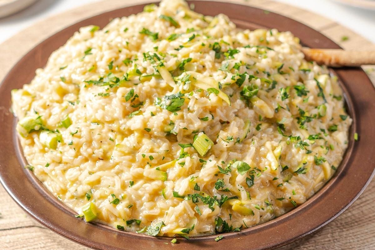 A plate of creamy risotto garnished with chopped herbs and green onions, served on a brown dish.
