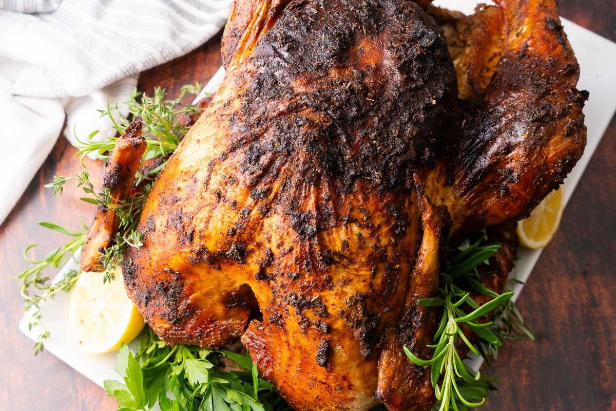 Whole roasted turkey with a spiced, crispy skin, garnished with fresh herbs and lemon slices on a platter.