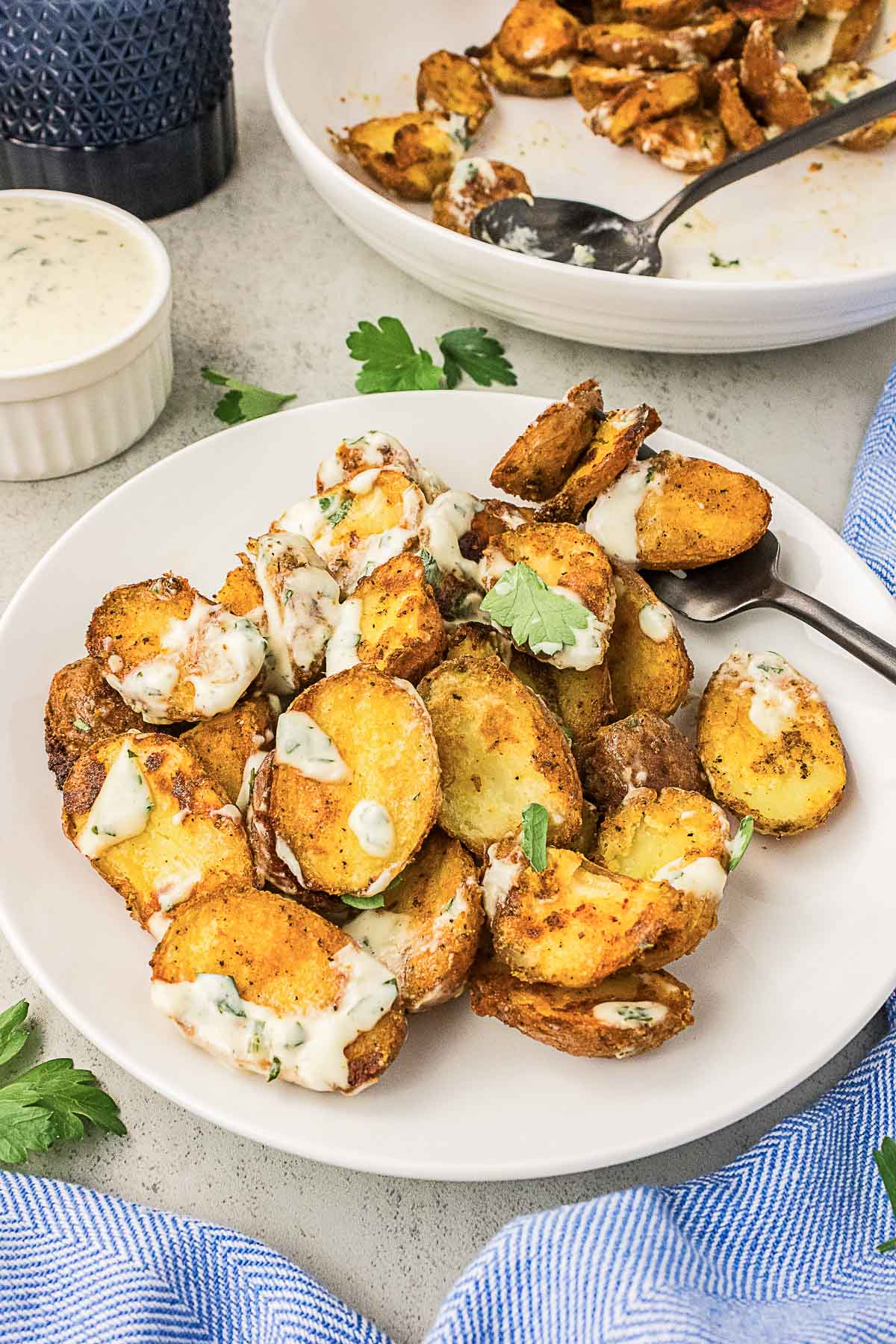 A plate of roasted potato slices garnished with creamy herb sauce, with a spoon, a ramekin of sauce, and parsley on the side.