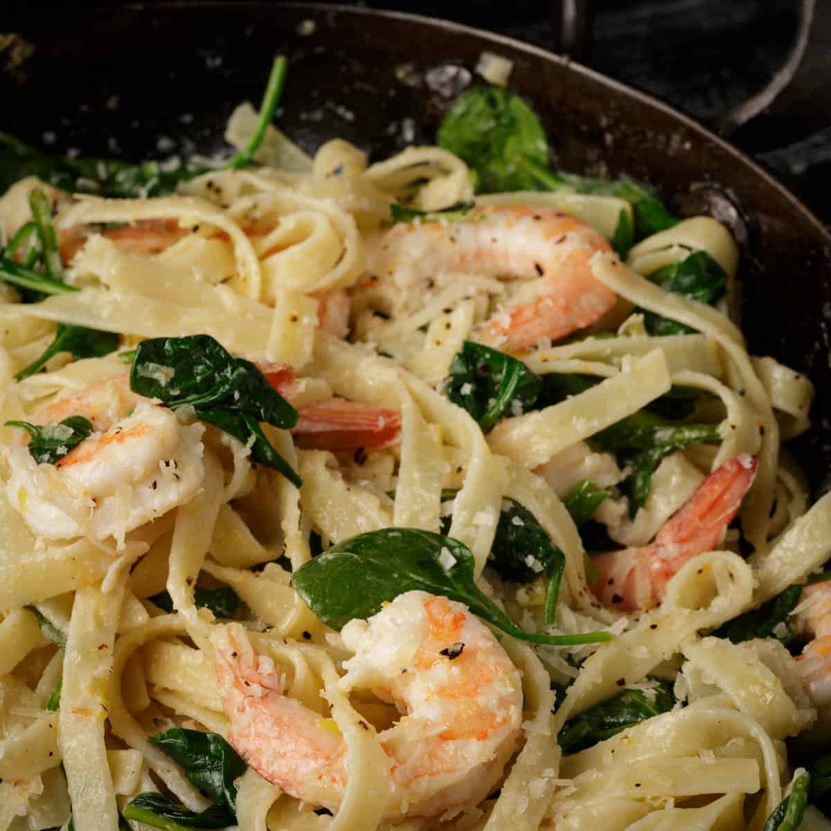 Fettuccine pasta with shrimp and spinach in a creamy sauce, served in a skillet.