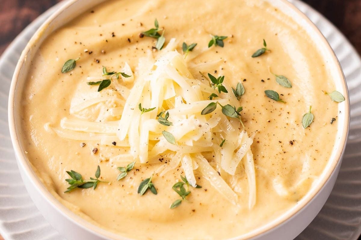 A bowl of creamy mashed potatoes topped with shredded cheese, fresh herbs, and cracked black pepper.