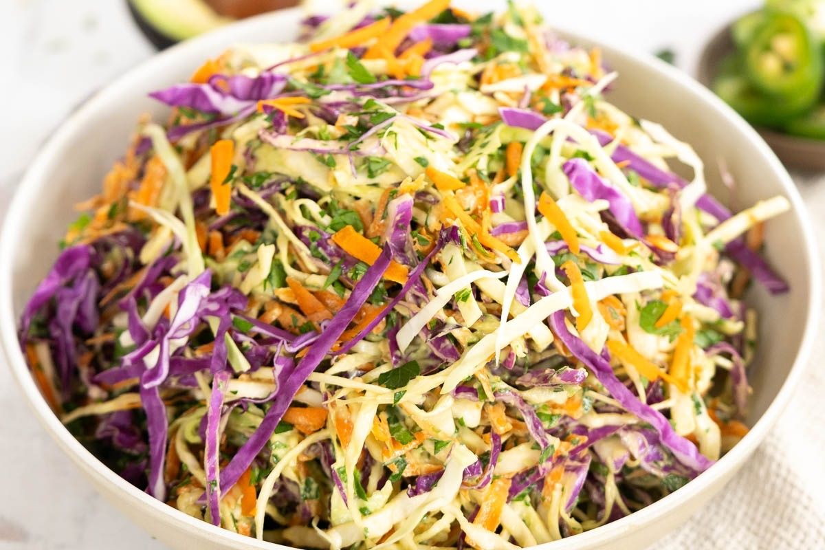 A bowl filled with coleslaw made of shredded green and purple cabbage, carrots, and fresh herbs, tossed in a creamy dressing.