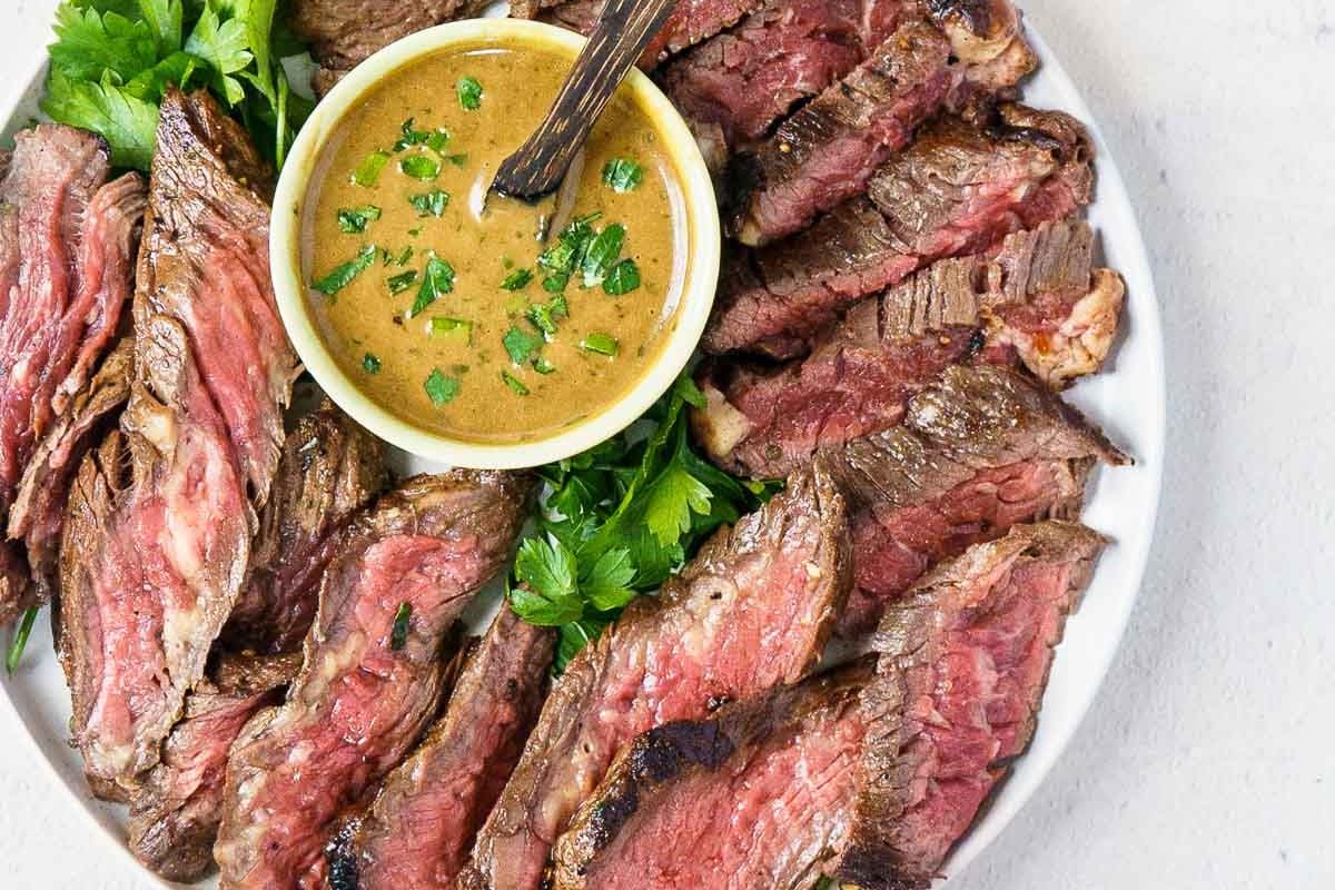 Plate of sliced medium-rare steak arranged around a small bowl of creamy sauce, garnished with fresh parsley.