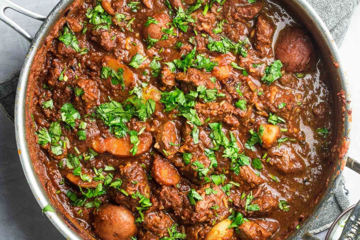 A pan filled with beef stew containing chunks of beef, potatoes, and carrots, garnished with chopped fresh parsley.