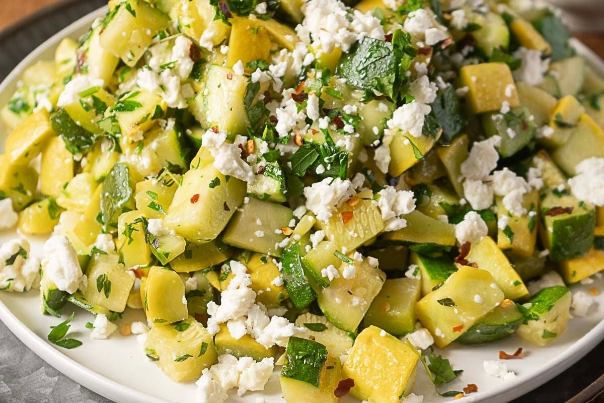 A plate of diced zucchini and yellow squash mixed with herbs and topped with crumbled feta cheese.