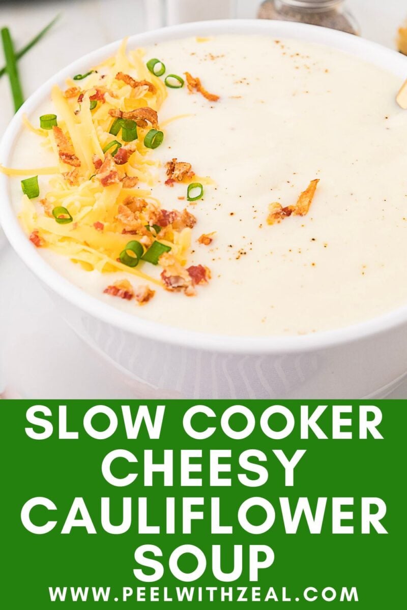 A bowl of creamy cheesy cauliflower soup topped with shredded cheese, bacon bits, and chopped green onions. Text over image reads, “Slow Cooker Cheesy Cauliflower Soup.”.