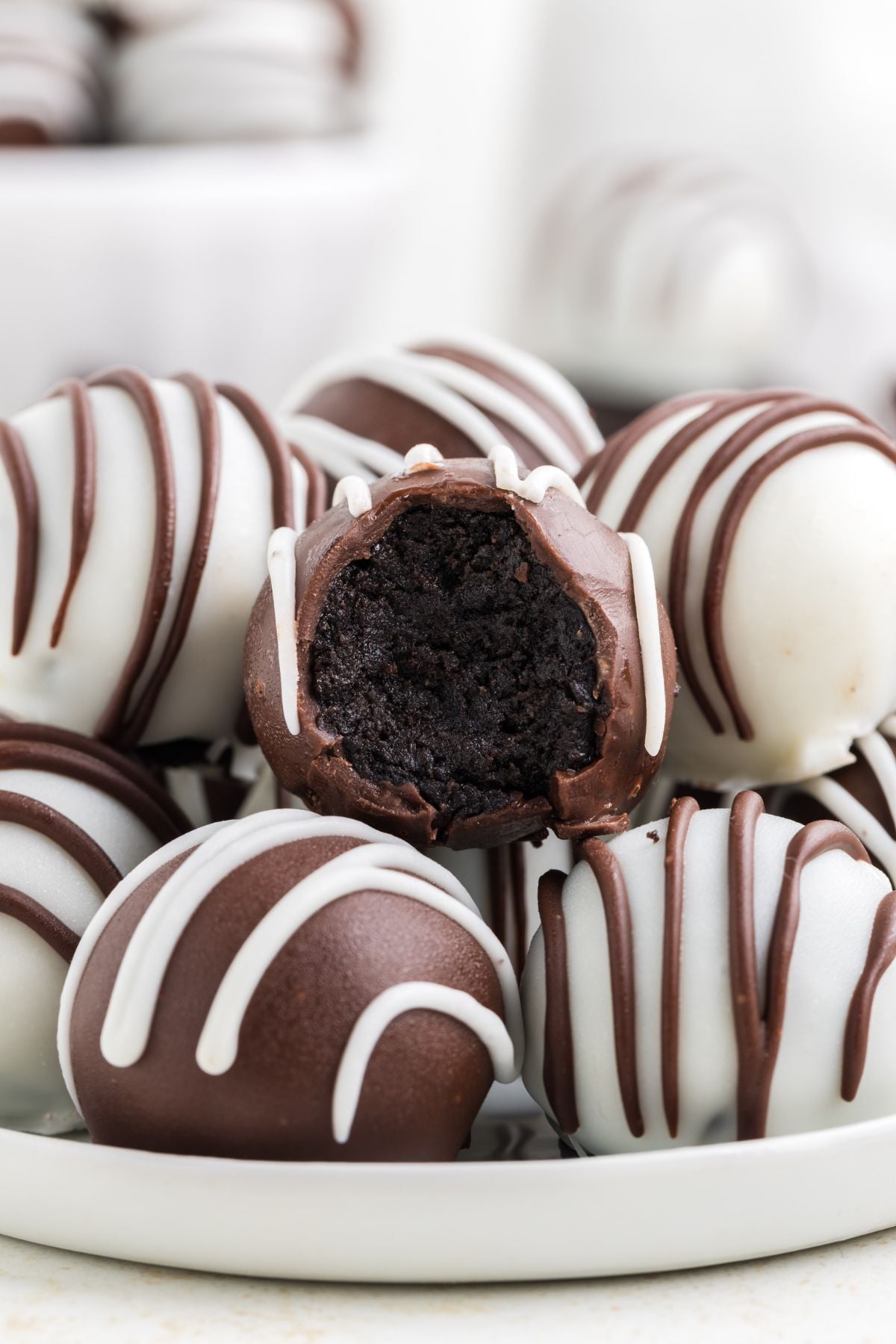 A plate of chocolate and white chocolate drizzled truffles, with one truffle partially bitten to reveal a dark chocolate filling