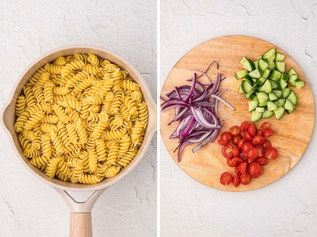 A saucepan with cooked rotini pasta sits on the left; on the right, a round wooden board holds sliced red onions, cucumbers, and halved cherry tomatoes.