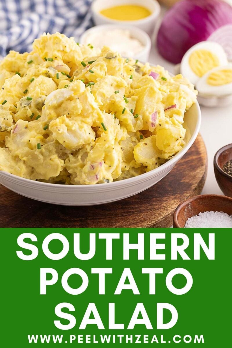 A bowl of Southern Potato Salad garnished with chives, featuring sliced boiled eggs and red onion, with condiments in the background.