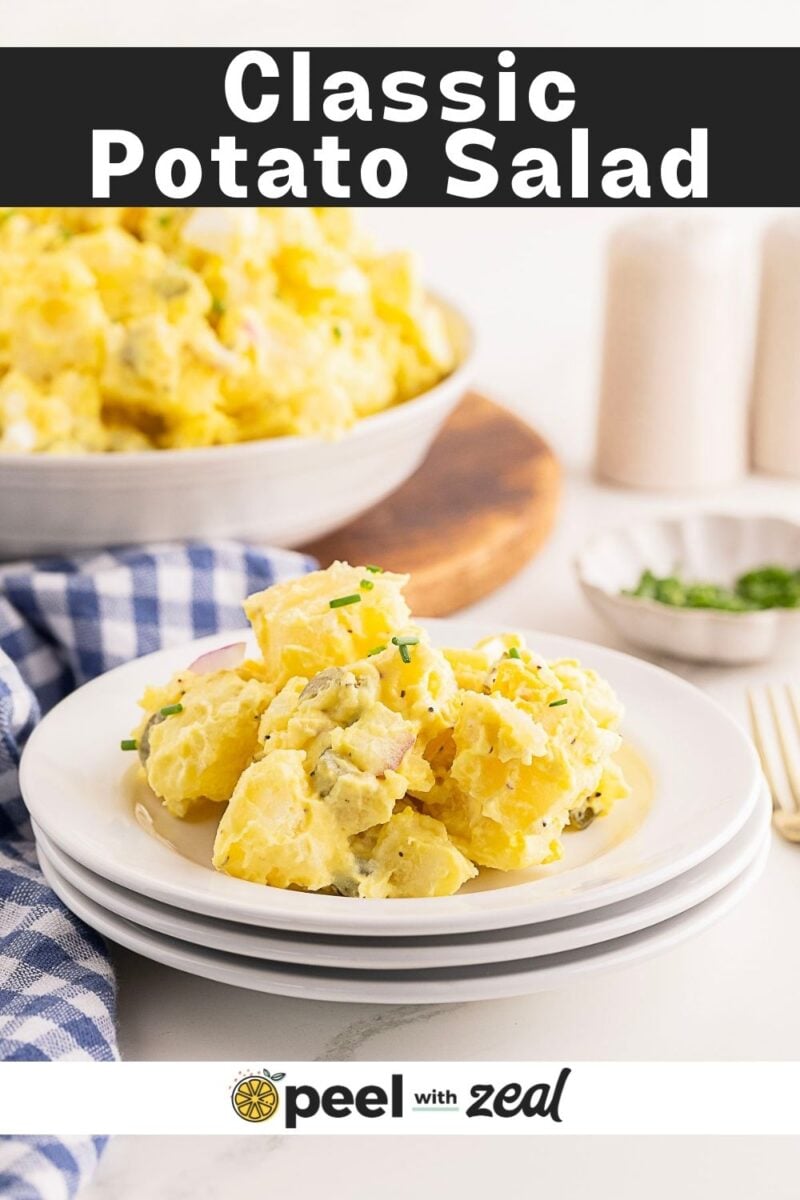 A serving of classic Southern Potato Salad on a white plate, with a larger bowl of potato salad and chopped herbs in the background.