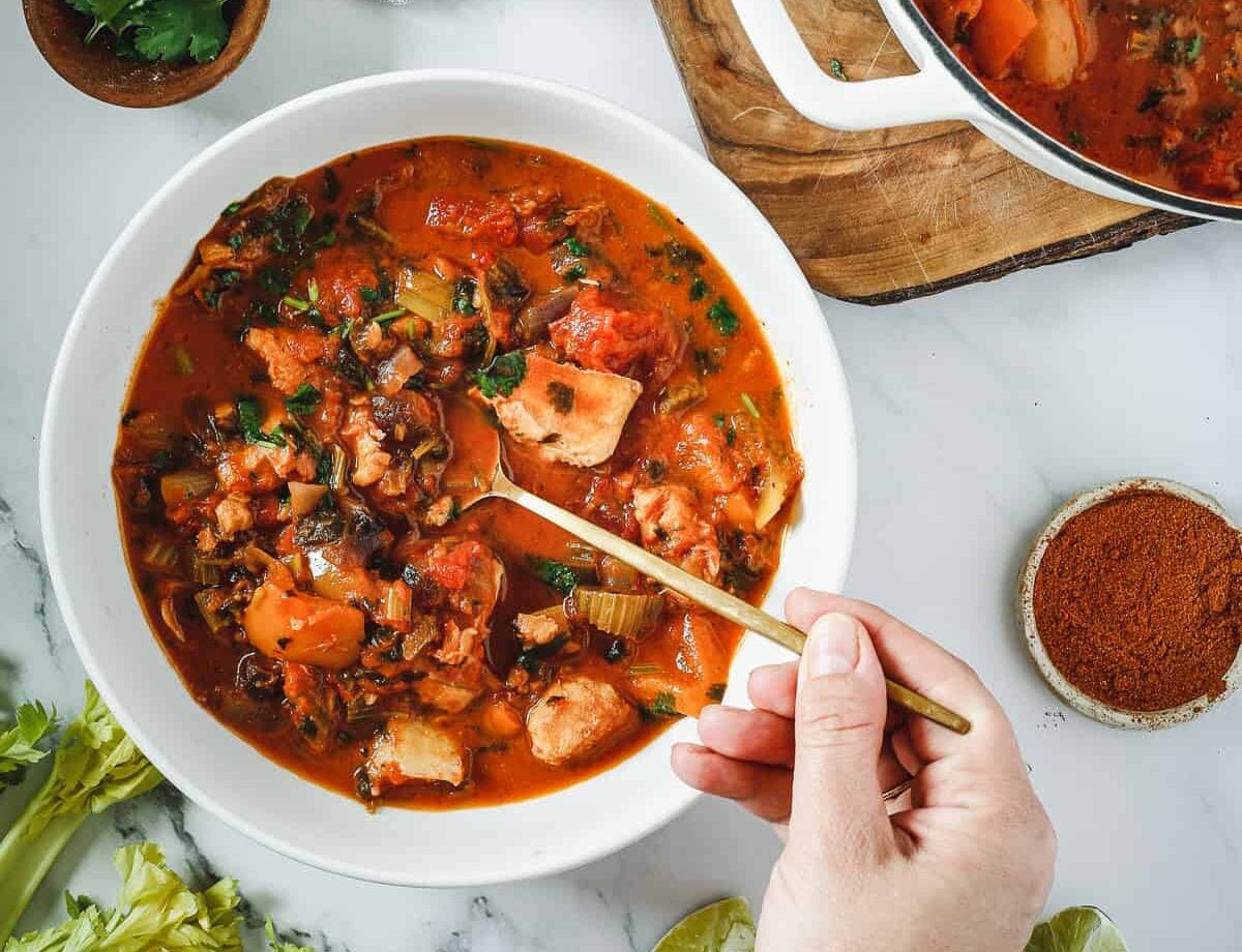 A bowl of hearty seafood stew with chunks of fish, tomatoes, celery, and herbs.