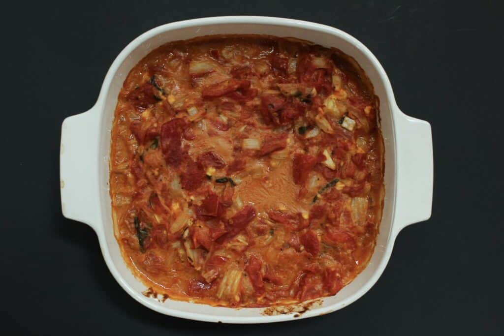 A white baking dish filled with a bubbling tomato and vegetable casserole.