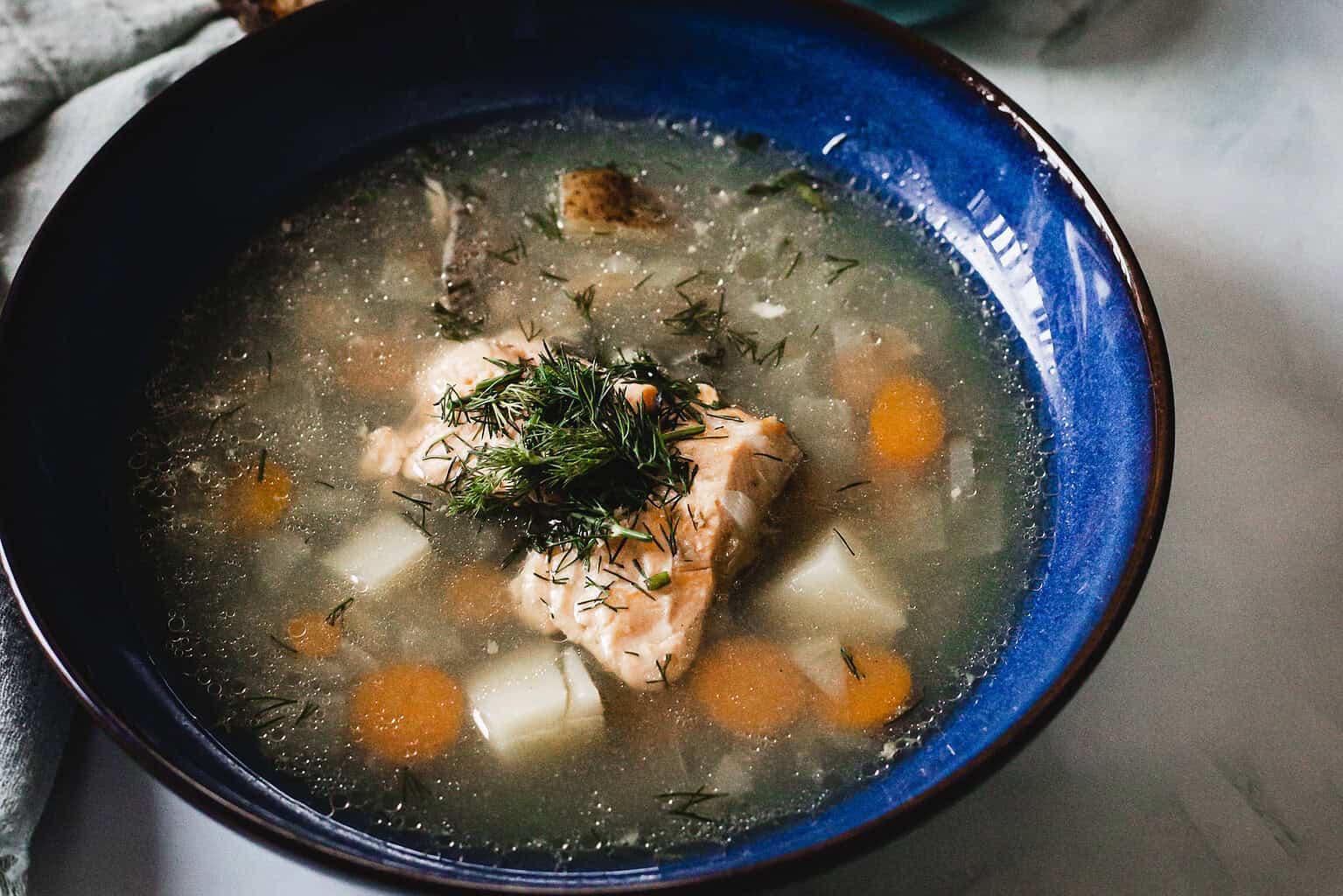 Salmon soup with potatoes, carrots, and dill in a blue bowl.