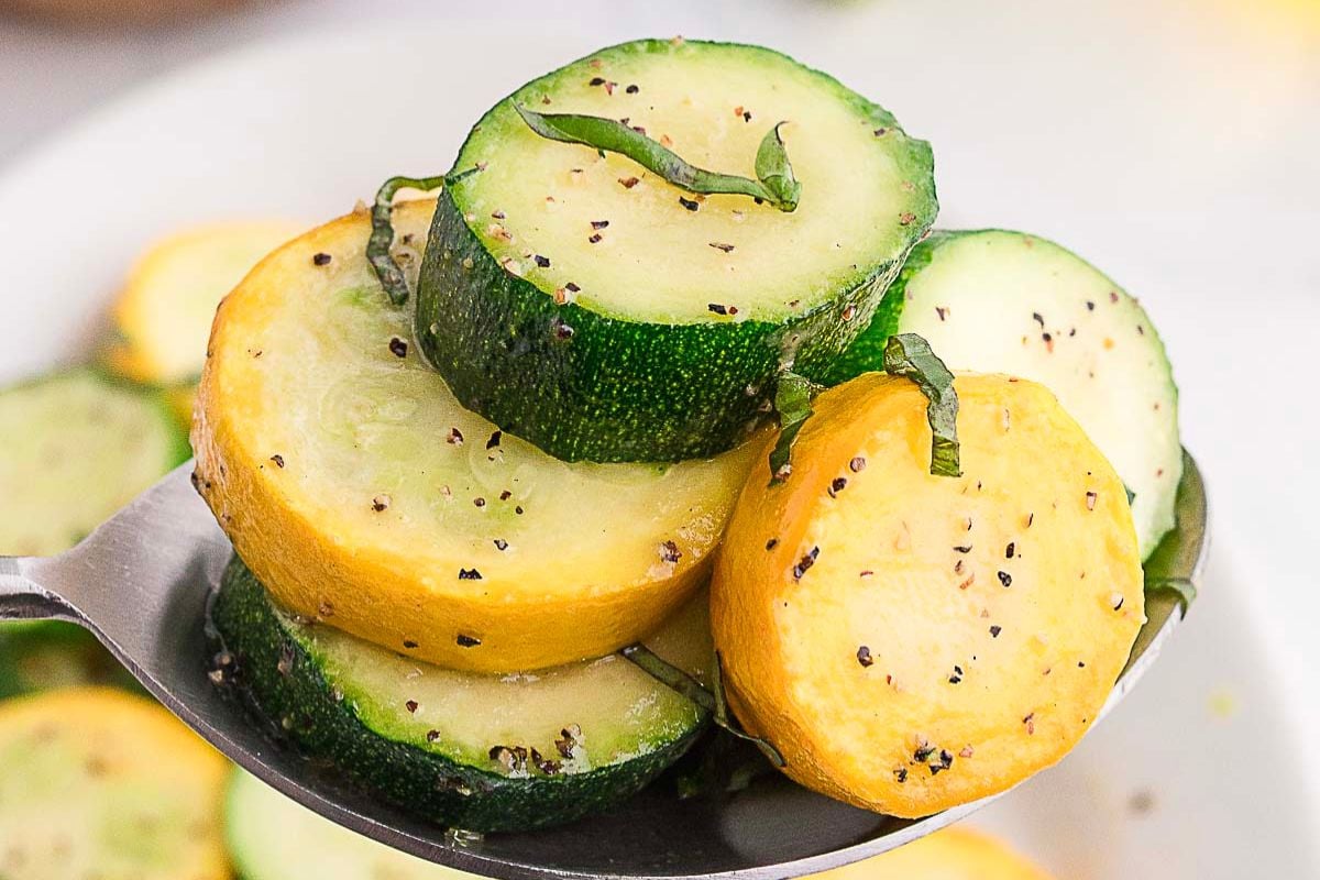 Sliced yellow squash and zucchini garnished with black pepper and herbs on a spoon&mdash;perfect for low-carb side dishes that are both flavorful and filling.