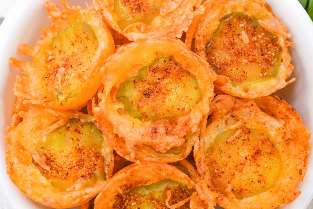 A close-up of several baked jalapeño slices topped with crispy melted cheese and sprinkled with chili powder, arranged in a white bowl.
