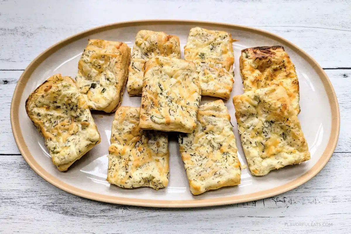 A plate with rectangular pieces of baked feta cheese garnished with herbs, arranged on a light-colored oval platter.