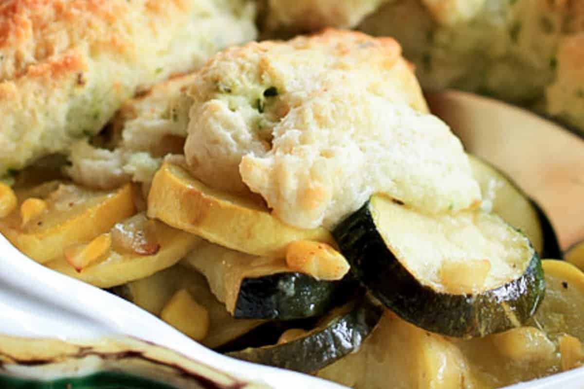 Close-up of a baked vegetable casserole, perfect for easy weeknight dinners, featuring sliced zucchini, yellow squash, onions, and a golden biscuit topping.