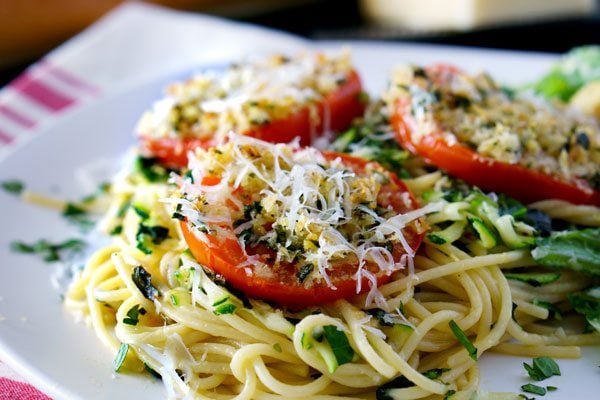 A plate of spaghetti topped with sliced roasted tomatoes, grated cheese, and chopped herbs.