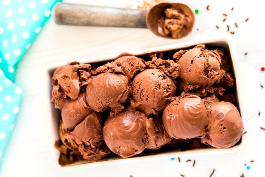 Rectangular dish filled with scoops of chocolate ice cream, with an ice cream scoop and blue polka dot cloth beside it.