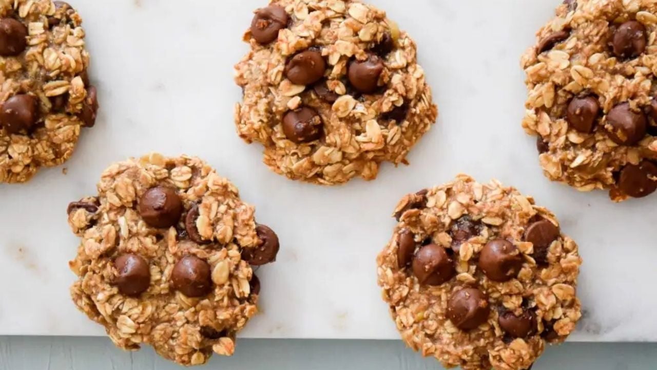 Five oatmeal cookies with chocolate chips are arranged on a white marble surface.